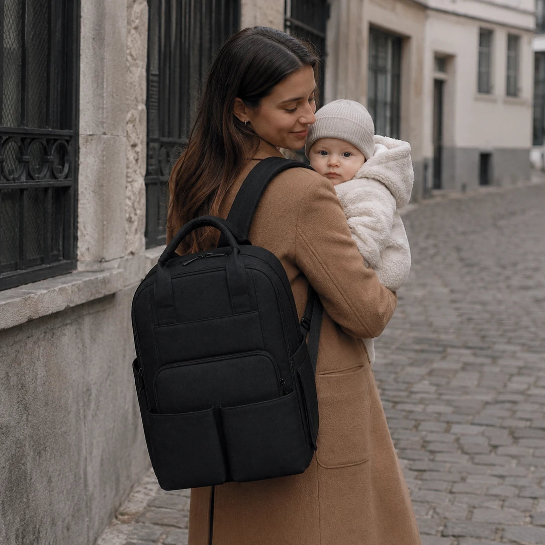 Sac à dos à langer compartimenté noir posé dans un salon lumineux | NOLIERA
